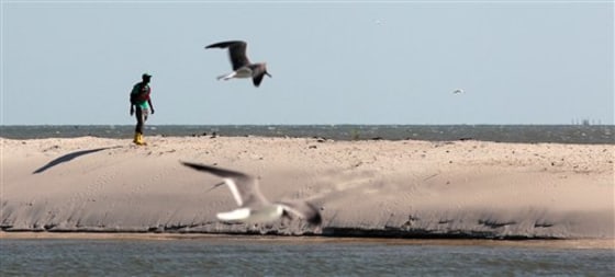 An oil cleanup worker walks along the beach in Dauphin Island, Ala. In Alabama's Dauphin Island, known for its sugar sand beaches and bird sanctuaries, 90 percent fewer people booked summer rentals compared to last summer, said Mayor Jeff Collier.